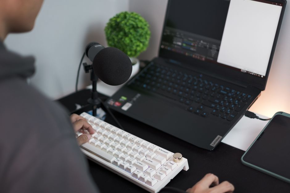 Microphone with a foam windscreen on a stand beside a laptop at a home desk